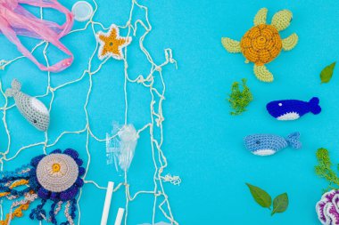 Dünya Okyanus Günü, su kirliliği farkındalığı ve çevresel eğitim görselleri. El yapımı tığ işi deniz hayvanları tek kullanımlık plastik eşyalar ve ağ, mavi arka plan, deri döşeme, üst görünüm