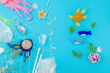 Dünya Okyanus Günü, su kirliliği farkındalığı ve çevresel eğitim görselleri. El yapımı tığ işi deniz hayvanları tek kullanımlık plastik eşyalar ve ağ, mavi arka plan, deri döşeme, üst görünüm