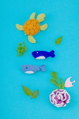 Dünya Okyanus Günü, su kirliliği farkındalığı ve çevresel eğitim görselleri. El yapımı tığ işi deniz hayvanları tek kullanımlık plastik eşyalar ve ağ, mavi arka plan, deri döşeme, üst görünüm
