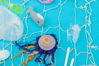 Dünya Okyanus Günü, su kirliliği farkındalığı ve çevresel eğitim görselleri. El yapımı tığ işi deniz hayvanları tek kullanımlık plastik eşyalar ve ağ, mavi arka plan, deri döşeme, üst görünüm