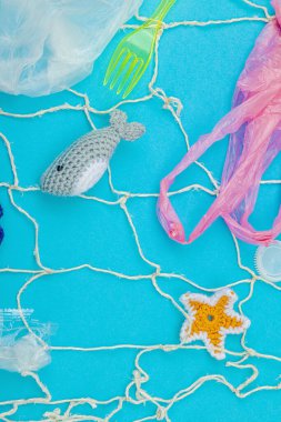 Dünya Okyanus Günü, su kirliliği farkındalığı ve çevresel eğitim görselleri. El yapımı tığ işi deniz hayvanları tek kullanımlık plastik eşyalar ve ağ, mavi arka plan, deri döşeme, üst görünüm