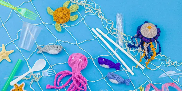 Dünya Okyanus Günü, su kirliliği farkındalığı ve çevresel eğitim görselleri. El yapımı tığ işi deniz hayvanları tek kullanımlık plastik eşyalar ve ağ, mavi arkaplan, deri döşeme, pankart formatında kapana kısıldılar.