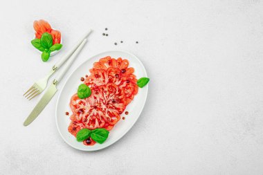 Dilimlenmiş Coeur de Boeuf domatesi, balzamik damlalar ve oval tabakta fesleğen yaprakları. Vejetaryen dostu, aile yadigarı, taş beton arka planda bir çiftlikten bir masaya estetik.