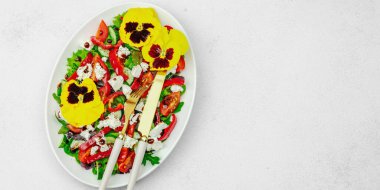 Domatesli taze vegan salatası, roka, keçi peyniri, zeytin ve beyaz tabakta yenilebilir çiçekler. Çevre dostu ve estetik titreşimli sağlıklı yemek konsepti. Beyaz arkaplan, pankart biçimi