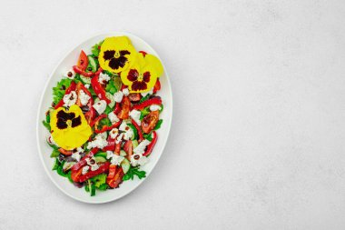 Domatesli taze vegan salatası, roka, keçi peyniri, zeytin ve beyaz tabakta yenilebilir çiçekler. Çevre dostu ve estetik titreşimli sağlıklı yemek konsepti. Beyaz arkaplan, üst görünüm