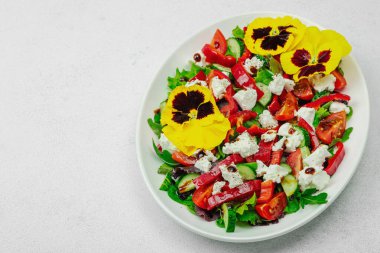 Domatesli taze vegan salatası, roka, keçi peyniri, zeytin ve beyaz tabakta yenilebilir çiçekler. Çevre dostu ve estetik titreşimli sağlıklı yemek konsepti. Beyaz arkaplan, alanı kopyala