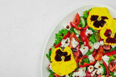 Domatesli taze vegan salatası, roka, keçi peyniri, zeytin ve beyaz tabakta yenilebilir çiçekler. Çevre dostu ve estetik titreşimli sağlıklı yemek konsepti. Beyaz arkaplan, kapat