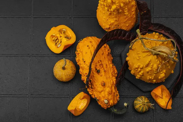 Dokulu derili organik süs balkabakları ve koyu arkaplanda dilimler. Doğal sebze konsepti, çiftlikten sofraya ve ekolojik gıda eğilimi, siyah arka plan, üst görünüm