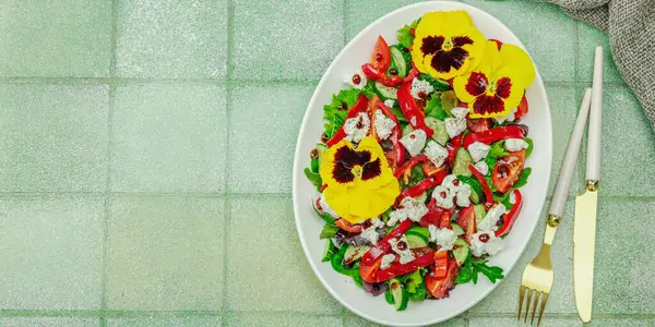 Domatesli taze vegan salatası, roka, keçi peyniri, zeytin ve beyaz tabakta yenilebilir çiçekler. Çevre dostu ve estetik titreşimli sağlıklı yemek konsepti. Moda kiremitleri arkaplan, pankart biçimi