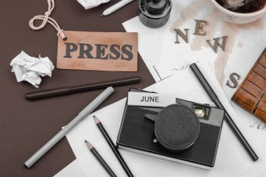 Klasik fotoğraf makinesi, basım etiketi, mürekkep şişesi dökülmüş kahve ve dağınık kağıtlarla yaratıcı bir daire. Gazeteciliğe, OSINT 'e ve gerçeğin peşinde koşmaya sembolik bir övgü.