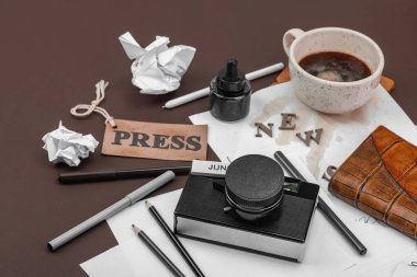 Klasik fotoğraf makinesi, basım etiketi, mürekkep şişesi dökülmüş kahve ve dağınık kağıtlarla yaratıcı bir daire. Gazeteciliğe, OSINT 'e ve gerçeğin peşinde koşmaya sembolik bir övgü.