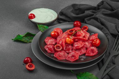 Koyu bir tabakta taze kiraz ve nane yapraklarıyla servis edilen ekşi kremalı kirazlı hamur tatlısı. Geleneksel Ukrayna tatlı tatlısı, düzlük, kopyalama alanı