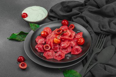 Koyu bir tabakta taze kiraz ve nane yapraklarıyla servis edilen ekşi kremalı kirazlı hamur tatlısı. Geleneksel Ukrayna tatlı tatlısı, düzlük, kopyalama alanı