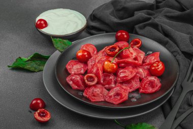 Koyu bir tabakta taze kiraz ve nane yapraklarıyla servis edilen ekşi kremalı kirazlı hamur tatlısı. Geleneksel Ukrayna tatlı tatlısı, düz uzanma, yakın çekim