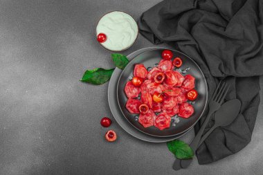 Koyu bir tabakta taze kiraz ve nane yapraklarıyla servis edilen ekşi kremalı kirazlı hamur tatlısı. Geleneksel Ukrayna tatlı tatlısı, düz uzanma, üst manzara