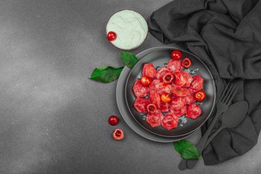 Koyu bir tabakta taze kiraz ve nane yapraklarıyla servis edilen ekşi kremalı kirazlı hamur tatlısı. Geleneksel Ukrayna tatlı tatlısı, düz uzanma, üst manzara