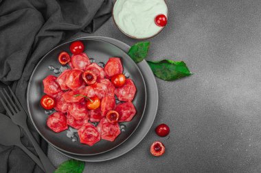 Koyu bir tabakta taze kiraz ve nane yapraklarıyla servis edilen ekşi kremalı kirazlı hamur tatlısı. Geleneksel Ukrayna tatlı tatlısı, düz uzanma, üst manzara