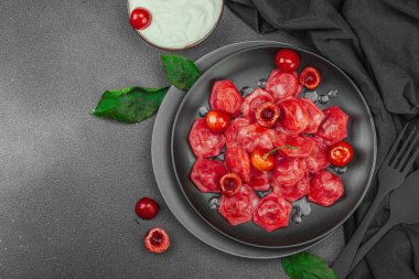 Koyu bir tabakta taze kiraz ve nane yapraklarıyla servis edilen ekşi kremalı kirazlı hamur tatlısı. Geleneksel Ukrayna tatlı tatlısı, düz uzanma, üst manzara