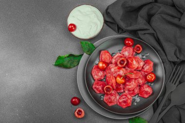 Koyu bir tabakta taze kiraz ve nane yapraklarıyla servis edilen ekşi kremalı kirazlı hamur tatlısı. Geleneksel Ukrayna tatlı tatlısı, düz uzanma, üst manzara