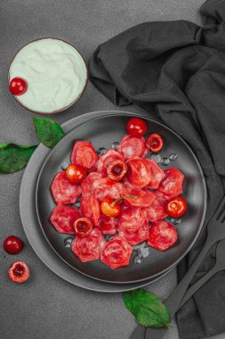 Koyu bir tabakta taze kiraz ve nane yapraklarıyla servis edilen ekşi kremalı kirazlı hamur tatlısı. Geleneksel Ukrayna tatlı tatlısı, düz uzanma, üst manzara