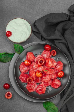 Koyu bir tabakta taze kiraz ve nane yapraklarıyla servis edilen ekşi kremalı kirazlı hamur tatlısı. Geleneksel Ukrayna tatlı tatlısı, düz uzanma, üst manzara