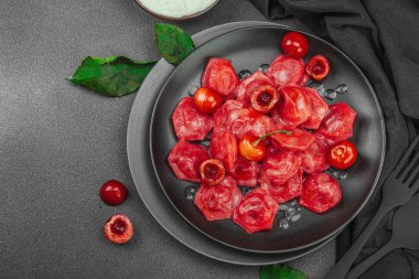 Koyu bir tabakta taze kiraz ve nane yapraklarıyla servis edilen ekşi kremalı kirazlı hamur tatlısı. Geleneksel Ukrayna tatlı tatlısı, düz uzanma, üst manzara