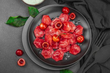 Koyu bir tabakta taze kiraz ve nane yapraklarıyla servis edilen ekşi kremalı kirazlı hamur tatlısı. Geleneksel Ukrayna tatlı tatlısı, düz uzanma, üst manzara