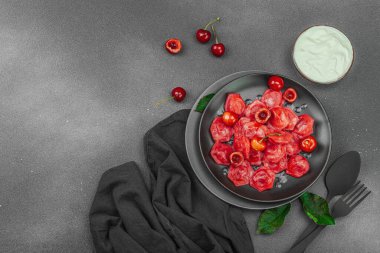 Koyu bir tabakta taze kiraz ve nane yapraklarıyla servis edilen ekşi kremalı kirazlı hamur tatlısı. Geleneksel Ukrayna tatlı tatlısı, düz uzanma, üst manzara