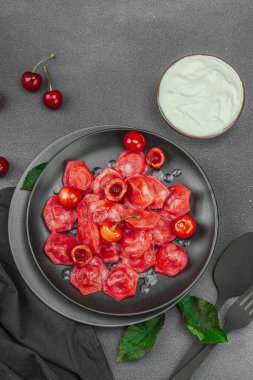 Koyu bir tabakta taze kiraz ve nane yapraklarıyla servis edilen ekşi kremalı kirazlı hamur tatlısı. Geleneksel Ukrayna tatlı tatlısı, düz uzanma, üst manzara