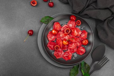 Koyu bir tabakta taze kiraz ve nane yapraklarıyla servis edilen ekşi kremalı kirazlı hamur tatlısı. Geleneksel Ukrayna tatlı tatlısı, düz uzanma, üst manzara