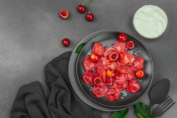 Koyu bir tabakta taze kiraz ve nane yapraklarıyla servis edilen ekşi kremalı kirazlı hamur tatlısı. Geleneksel Ukrayna tatlı tatlısı, düz uzanma, üst manzara