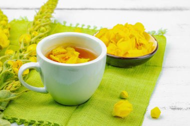 Bir fincan çiçekli ve yapraklı bitki çayı. Doğal ışık, alternatif tıp, klasik şifalı bitki havası, ahşap arka plan, kopyalama alanı