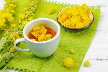 Bir fincan çiçekli ve yapraklı bitki çayı. Doğal ışık, alternatif tıp, klasik şifalı bitki havası, ahşap arka plan, kopyalama alanı