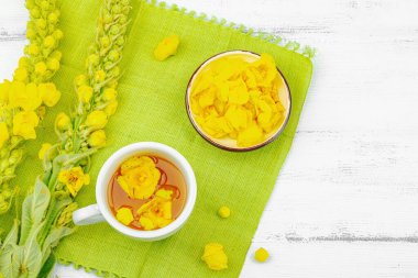 Bir fincan çiçekli ve yapraklı bitki çayı. Doğal ışık, alternatif tıp, klasik şifalı bitki havası, ahşap arka plan, üst görünüm