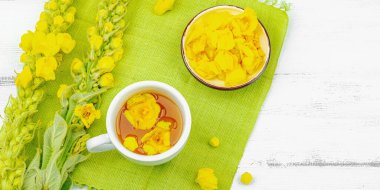 Bir fincan çiçekli ve yapraklı bitki çayı. Doğal ışık, alternatif tıp, antika şifalı bitkiler, ahşap arka plan, afiş biçimi