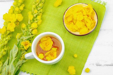 Bir fincan çiçekli ve yapraklı bitki çayı. Doğal ışık, alternatif tıp, klasik şifalı bitki havası, ahşap arka plan, üst görünüm