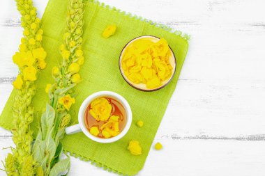 Bir fincan çiçekli ve yapraklı bitki çayı. Doğal ışık, alternatif tıp, klasik şifalı bitki havası, ahşap arka plan, üst görünüm