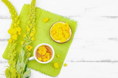 Bir fincan çiçekli ve yapraklı bitki çayı. Doğal ışık, alternatif tıp, klasik şifalı bitki havası, ahşap arka plan, üst görünüm