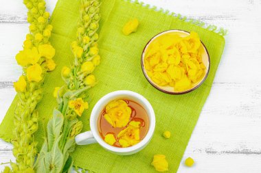 Bir fincan çiçekli ve yapraklı bitki çayı. Doğal ışık, alternatif tıp, klasik şifalı bitki havası, ahşap arka plan, üst görünüm