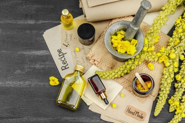 Verbascum çiçekleriyle doğal cilt bakımı, yağlar, kremler ve güzellik tedavileri için bitkisel malzeme. Siyah ahşap arkaplan, üst manzara