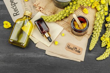 Verbascum çiçekleriyle doğal cilt bakımı, yağlar, kremler ve güzellik tedavileri için bitkisel malzeme. Siyah ahşap arkaplan, üst manzara