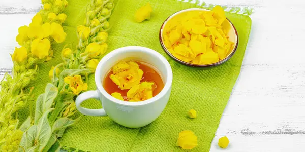 Bir fincan çiçekli ve yapraklı bitki çayı. Doğal ışık, alternatif tıp, antika şifalı bitkiler, ahşap arka plan, afiş biçimi