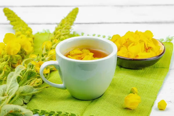 Bir fincan çiçekli ve yapraklı bitki çayı. Doğal ışık, alternatif tıp, klasik şifalı bitki havası, ahşap arka plan, kopyalama alanı