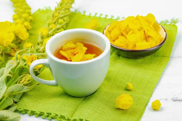 Bir fincan çiçekli ve yapraklı bitki çayı. Doğal ışık, alternatif tıp, klasik şifalı bitki havası, ahşap arka plan, kopyalama alanı