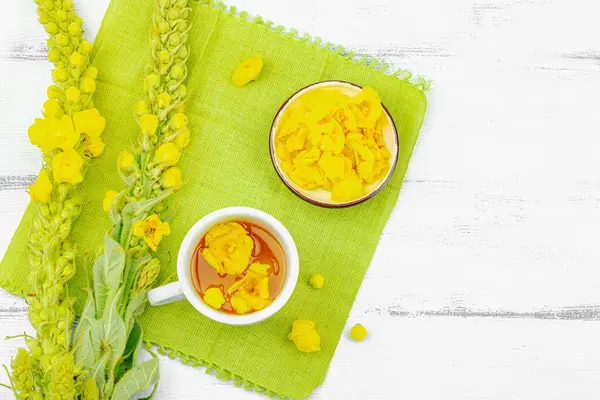 Bir fincan çiçekli ve yapraklı bitki çayı. Doğal ışık, alternatif tıp, klasik şifalı bitki havası, ahşap arka plan, üst görünüm