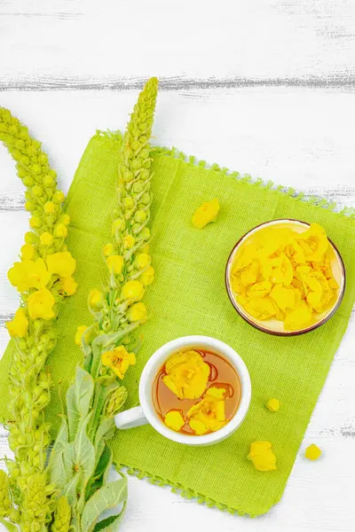 Bir fincan çiçekli ve yapraklı bitki çayı. Doğal ışık, alternatif tıp, klasik şifalı bitki havası, ahşap arka plan, üst görünüm