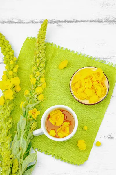 Bir fincan çiçekli ve yapraklı bitki çayı. Doğal ışık, alternatif tıp, klasik şifalı bitki havası, ahşap arka plan, üst görünüm