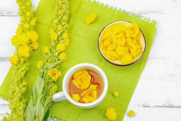 Bir fincan çiçekli ve yapraklı bitki çayı. Doğal ışık, alternatif tıp, klasik şifalı bitki havası, ahşap arka plan, üst görünüm