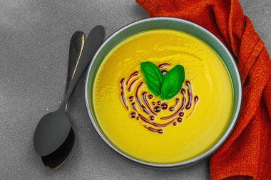 Fesleğen ve balzamik jöleli kremalı kabak çorbası taze malzemeler ve baharatlarla moda bir kasede servis ediliyor. Koyu taş zemin, üst görünüm