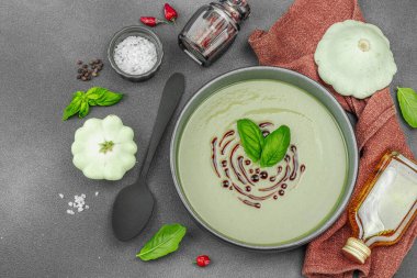Fesleğen ve balzamik jöleli kremalı kabak çorbası taze malzemeler ve baharatlarla moda bir kasede servis ediliyor. Koyu taş zemin, üst görünüm